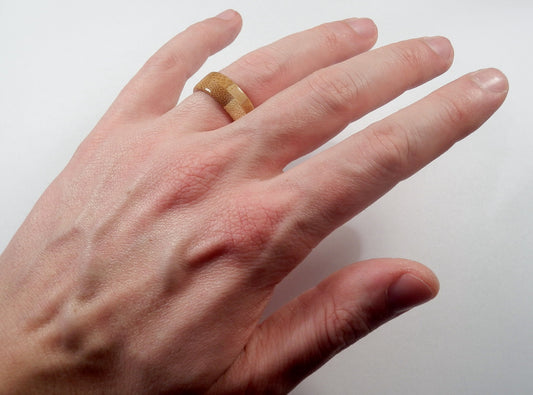 A close-up of a person's hand wearing a handmade bamboo ring on the ring finger, set against a plain light background.
