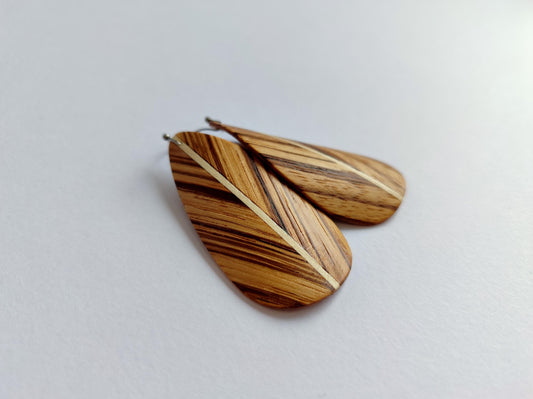 A pair of teardrop zebrano wooden earrings with a natural wood grain pattern and a light beige stripe down the center, displayed on a light gray background.