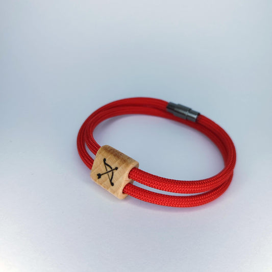 A red braided cord bracelet with a natural wood square charm engraved with a black symbol, set against a plain light gray background.