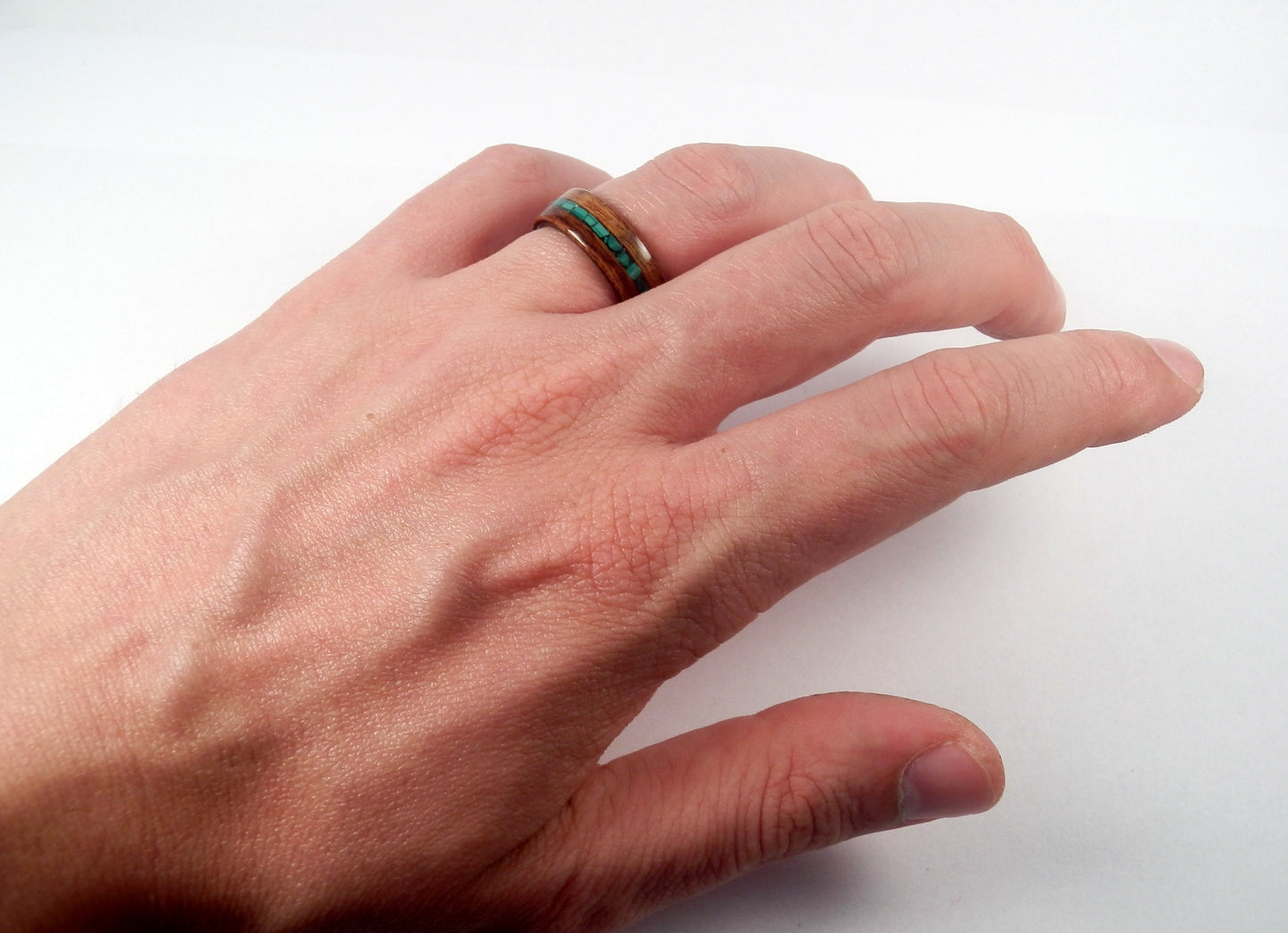 A close-up of a person's hand wearing a ring with a dark brown wood inlay and a malachite green stone accent, set against a plain white background.