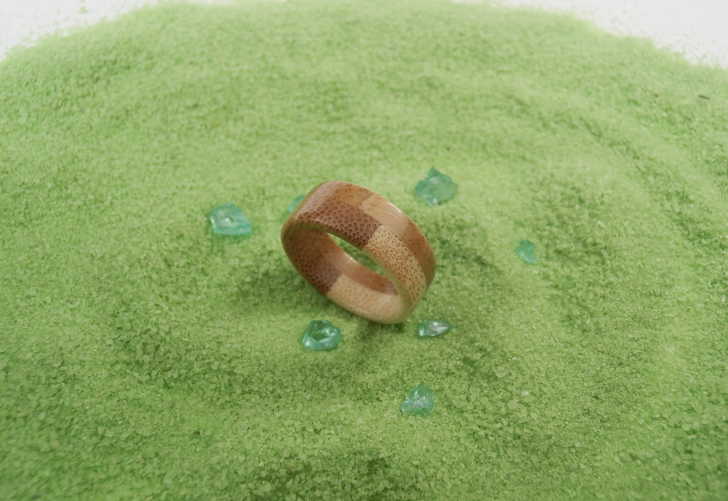 A wooden ring with a natural brown and beige striped pattern rests on a mound of bright green powder, surrounded by a few scattered translucent green crystals.