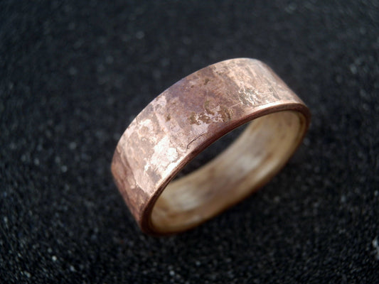 A hammer textured copper ring band with a metallic finish, photographed on a dark textured background.