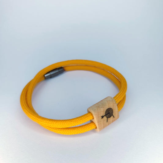 A yellow braided cord bracelet with a natural wood toggle featuring a black engraved archery target design, photographed on a light gray background.