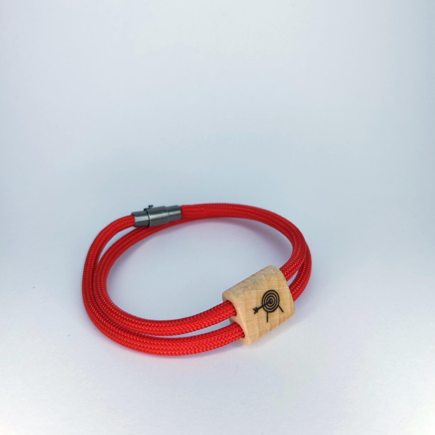 A red braided cord bracelet with a silver metal clasp and a light wood spacer featuring a black engraved target design, shown on a light gray background.
