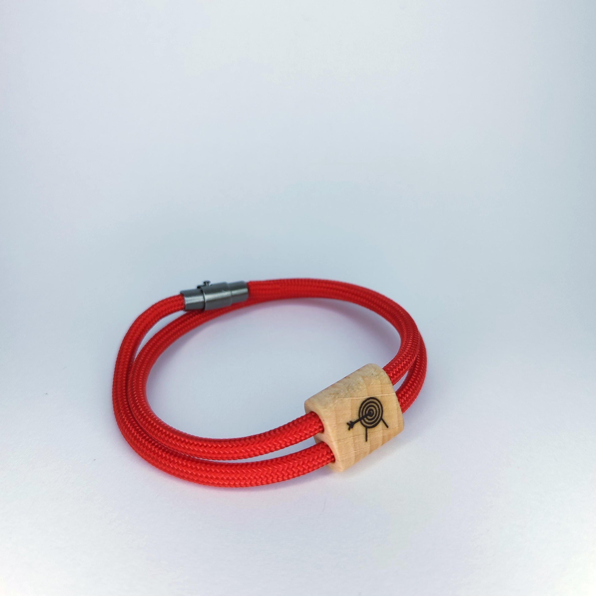 A red braided cord bracelet with a silver metal clasp and a light wood spacer featuring a black engraved target design, shown on a light gray background.