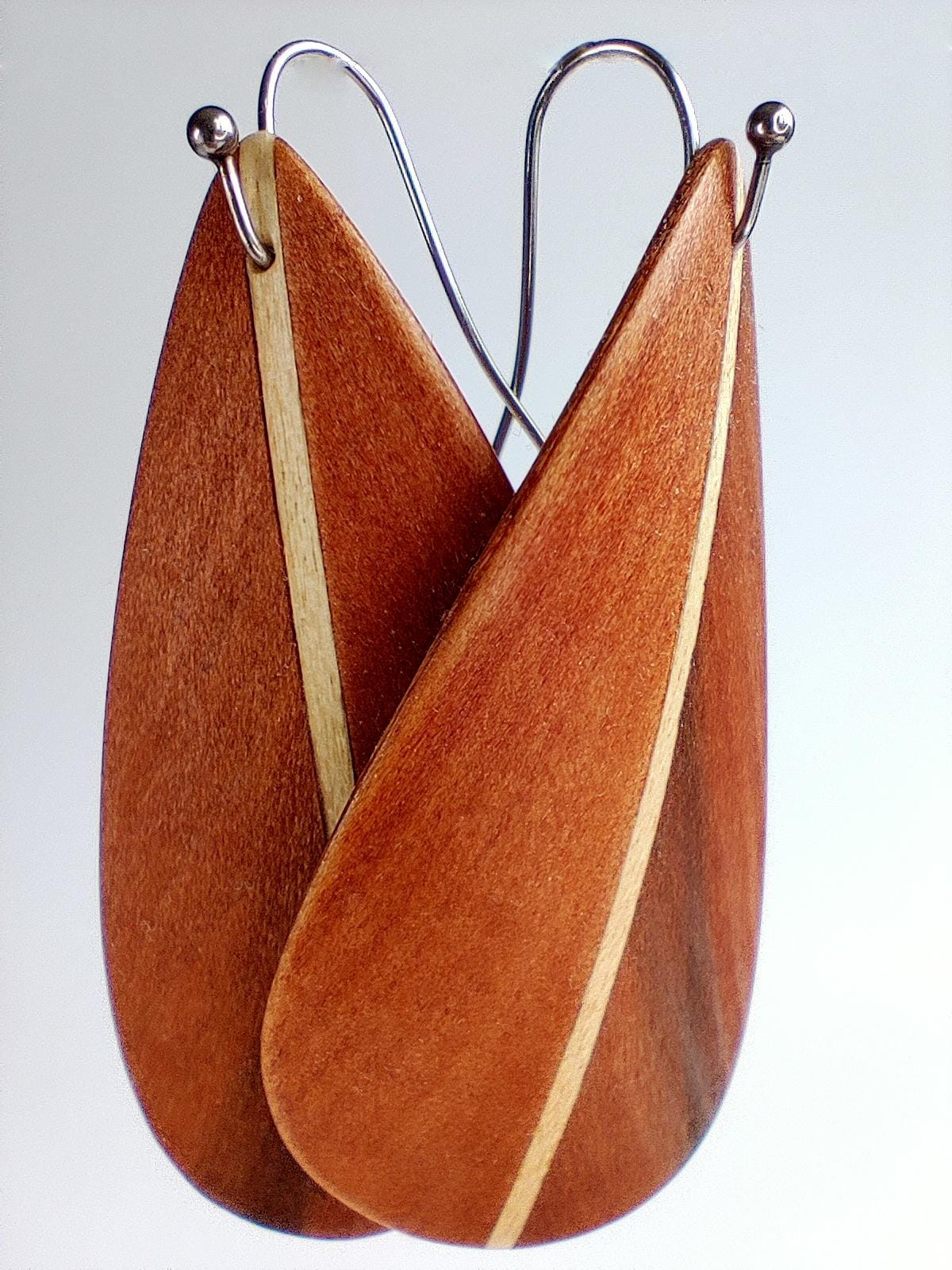 Wooden teardrop-shaped  feather inspired design earrings with a natural wood grain pattern and a light-colored inlay, suspended from silver-tone wire hooks.