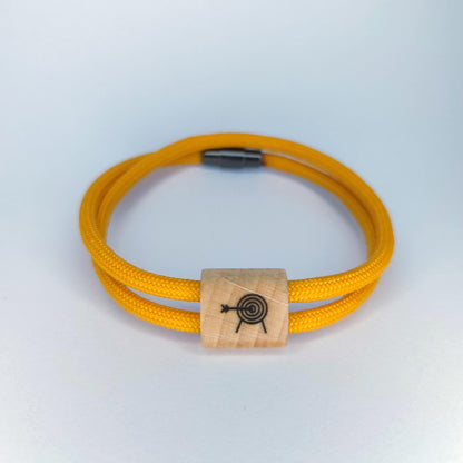 A yellow paracord bracelet with a rectangular light wood bead featuring a black engraved  archery target design, shown on a light gray background.