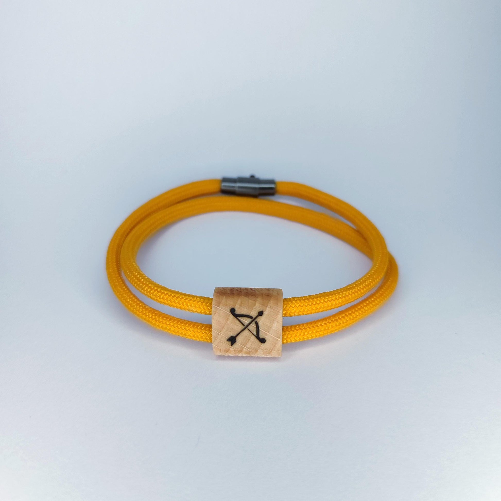 A double-strand yellow paracord bracelet with a square natural wood charm featuring a bow engraved symbol, set against a light gray background.