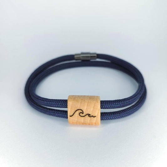 A double-strand navy blue braided cord bracelet with a natural light wood square bead engraved with a black wave design, shown on a light gray background.