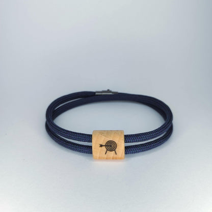A dark navy blue paracord bracelet with a square natural wood bead engraved with a archery target design, shown on a light gray background.