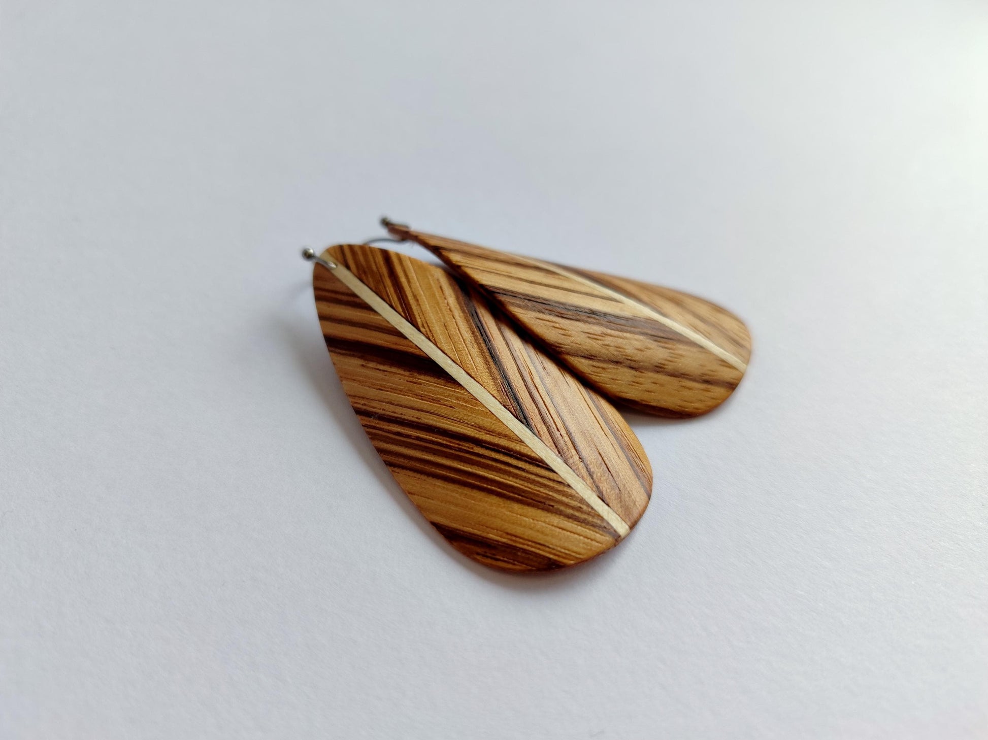 A pair of teardrop zebrano wooden earrings with a natural wood grain pattern and a light beige stripe down the center, displayed on a light gray background.