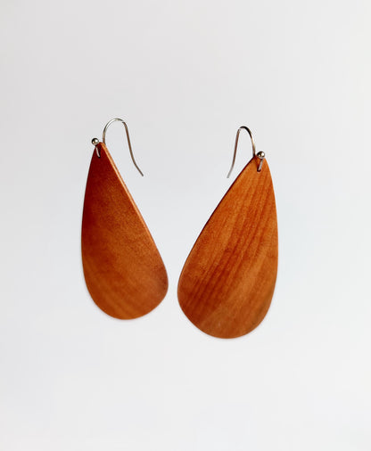 A pair of teardrop-shaped wooden drop earrings with a warm reddish-brown wood grain finish and silver-tone fishhook wires, shown against a plain light gray background.