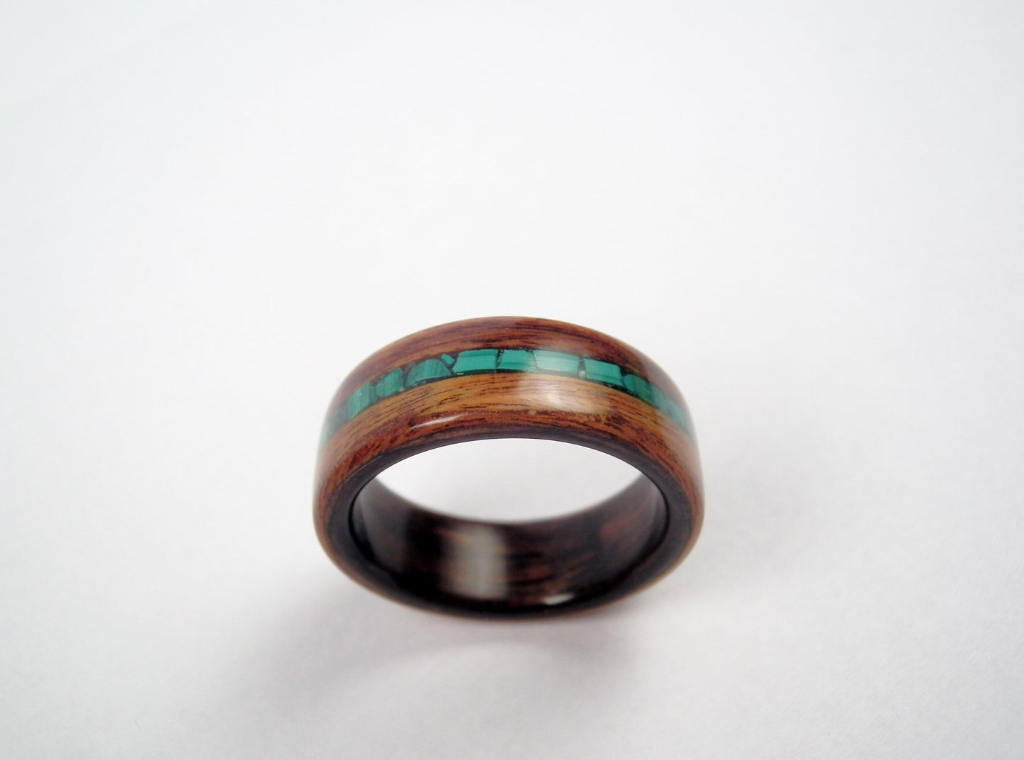 A rosewood wooden ring band with a polished dark brown finish and a central inlay of malachite stones, shown on a plain light background.