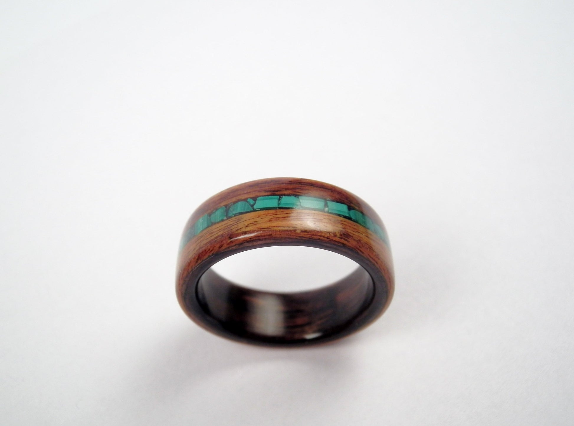 A rosewood wooden ring band with a polished dark brown finish and a central inlay of malachite stones, shown on a plain light background.