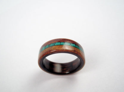 A rosewood wooden ring band with a polished dark brown finish and a central inlay of malachite stones, shown on a plain light background.
