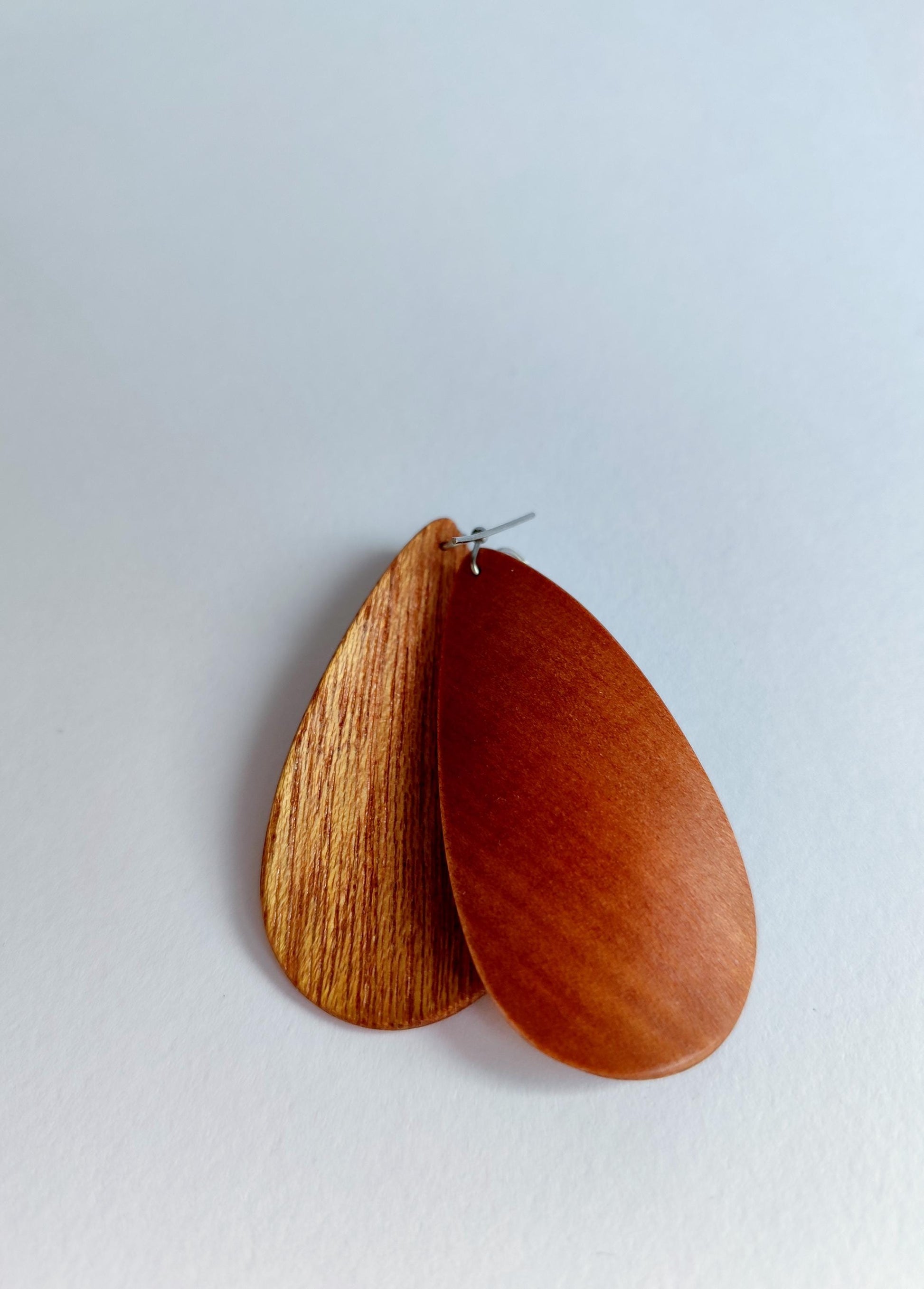 A pair of teardrop-shaped wooden earrings with silver posts, displayed on a light gray background.