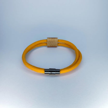 A yellow braided cord bracelet with a light wood accent and a silver metal magnetic clasp, displayed on a light blue-gray gradient background.