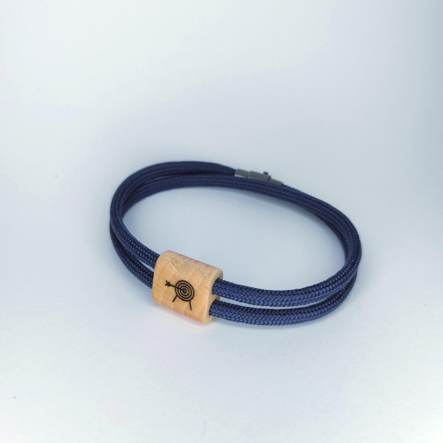 A navy blue braided cord bracelet with a rectangular light wood accent bead featuring a black laser-engraved target design, shown on a light gray background.