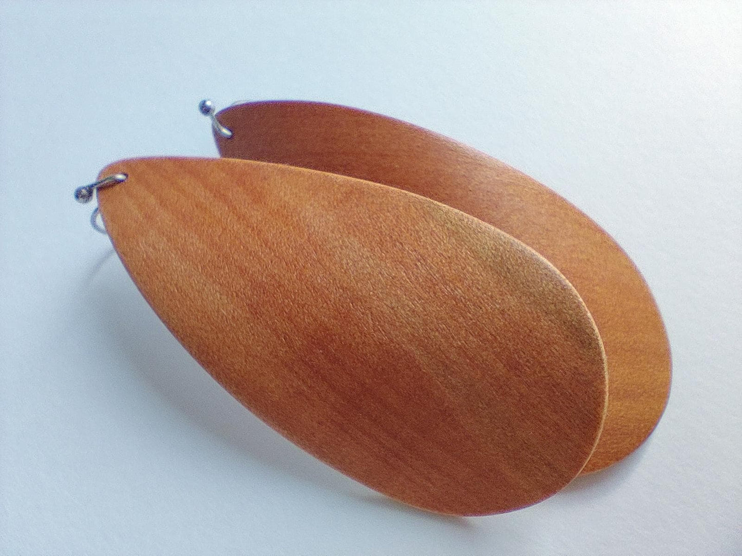 A pair of large, teardrop-shaped wooden earrings with a warm reddish-brown finish and visible wood grain, displayed on a light gray background.