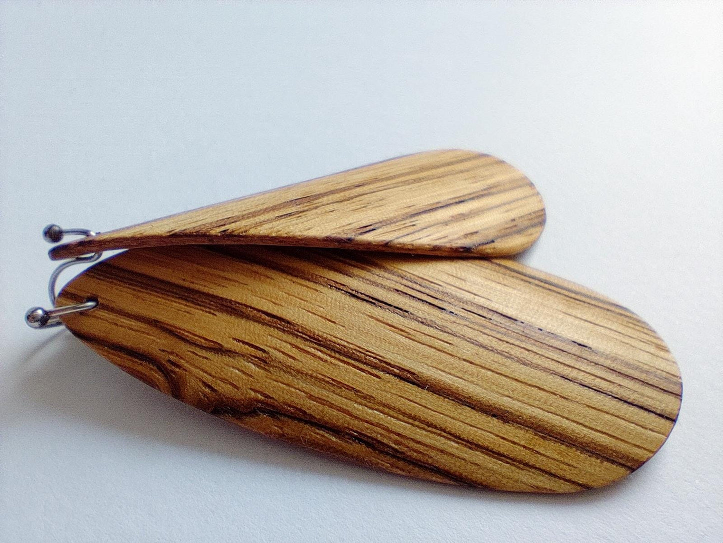 A pair of large, teardrop-shaped wooden earrings with a natural zebra wood grain pattern, attached to silver-tone metal posts, shown on a plain light background.