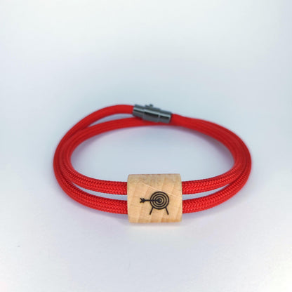 A red braided cord bracelet with a rectangular light wood bead engraved with a black target design, shown on a plain white background.