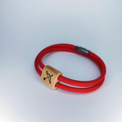 A red braided cord bracelet with a natural wood square charm engraved with a black symbol, set against a plain light gray background.