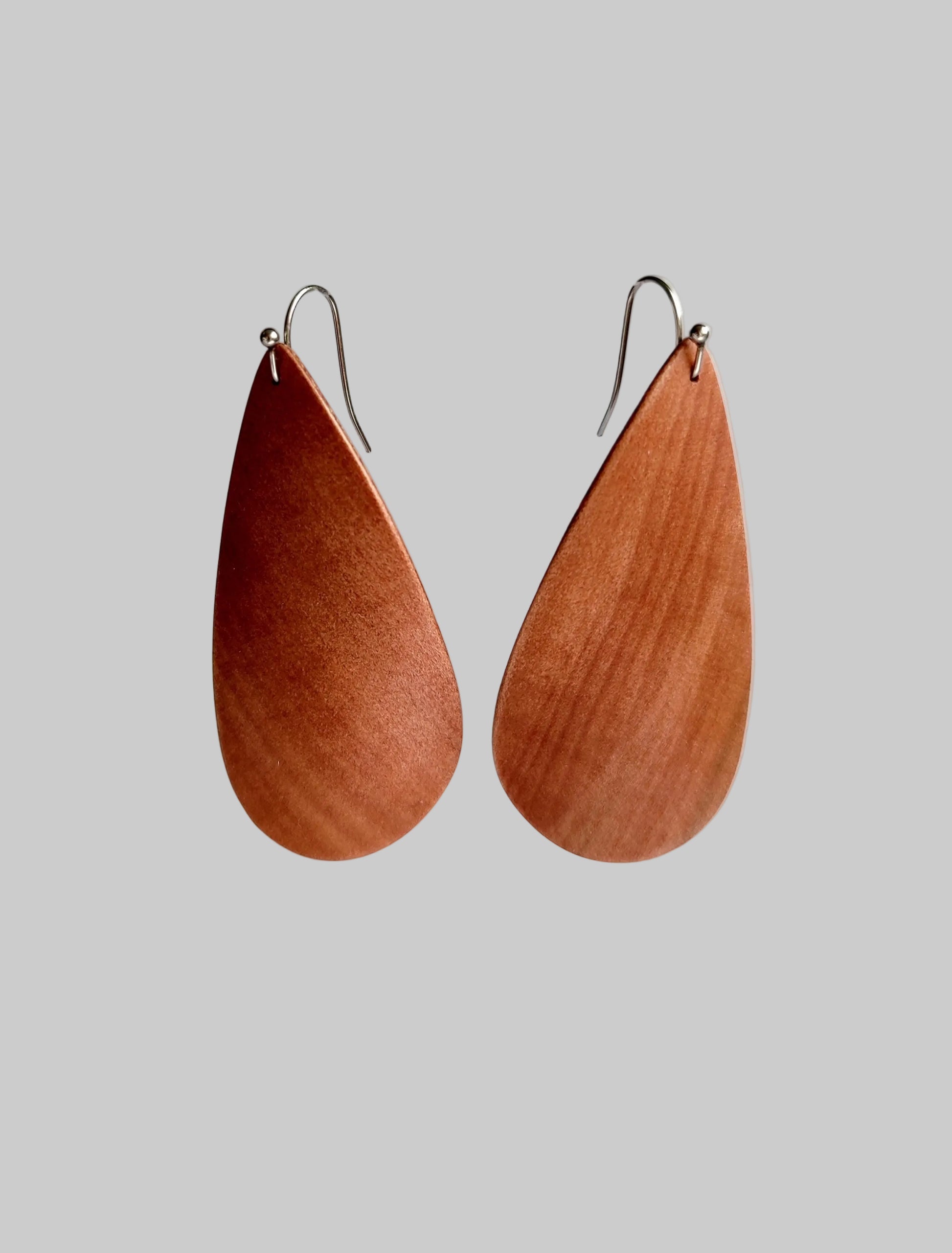 A pair of teardrop-shaped wooden drop earrings with silver fishhook wires, displayed against a clean, light gray background.