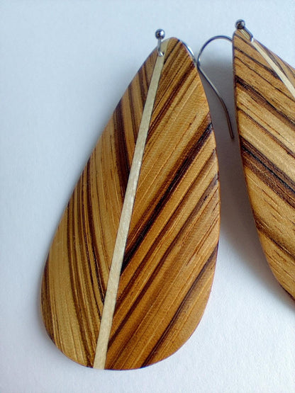 Teardrop-shaped wooden drop earrings with a natural wood grain pattern, featuring a central light beige stripe and silver fishhook wires, shown against a plain off-white background.