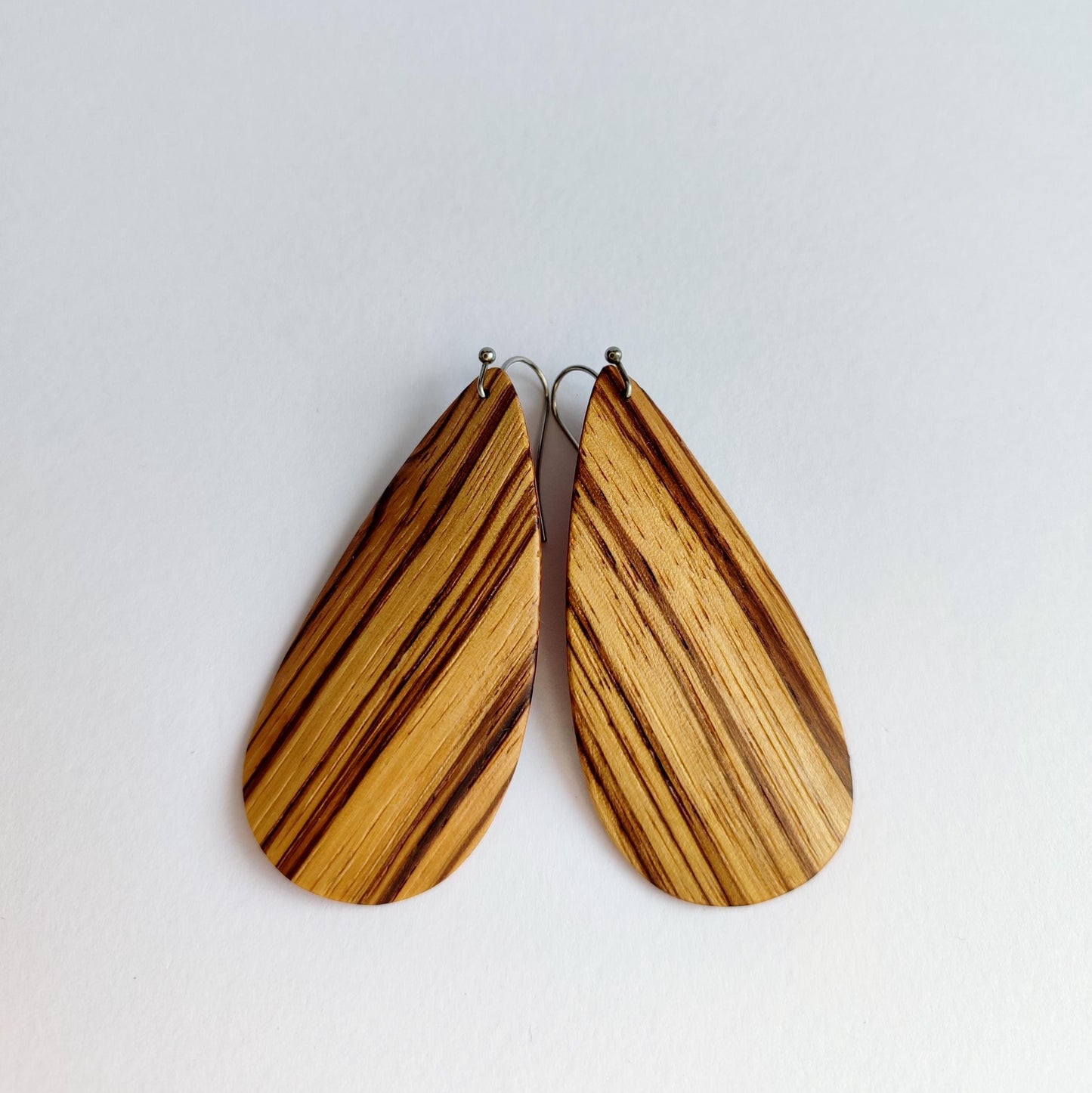 A pair of teardrop-shaped wooden drop earrings with a natural zebra wood grain pattern, hanging against a plain light gray background.
