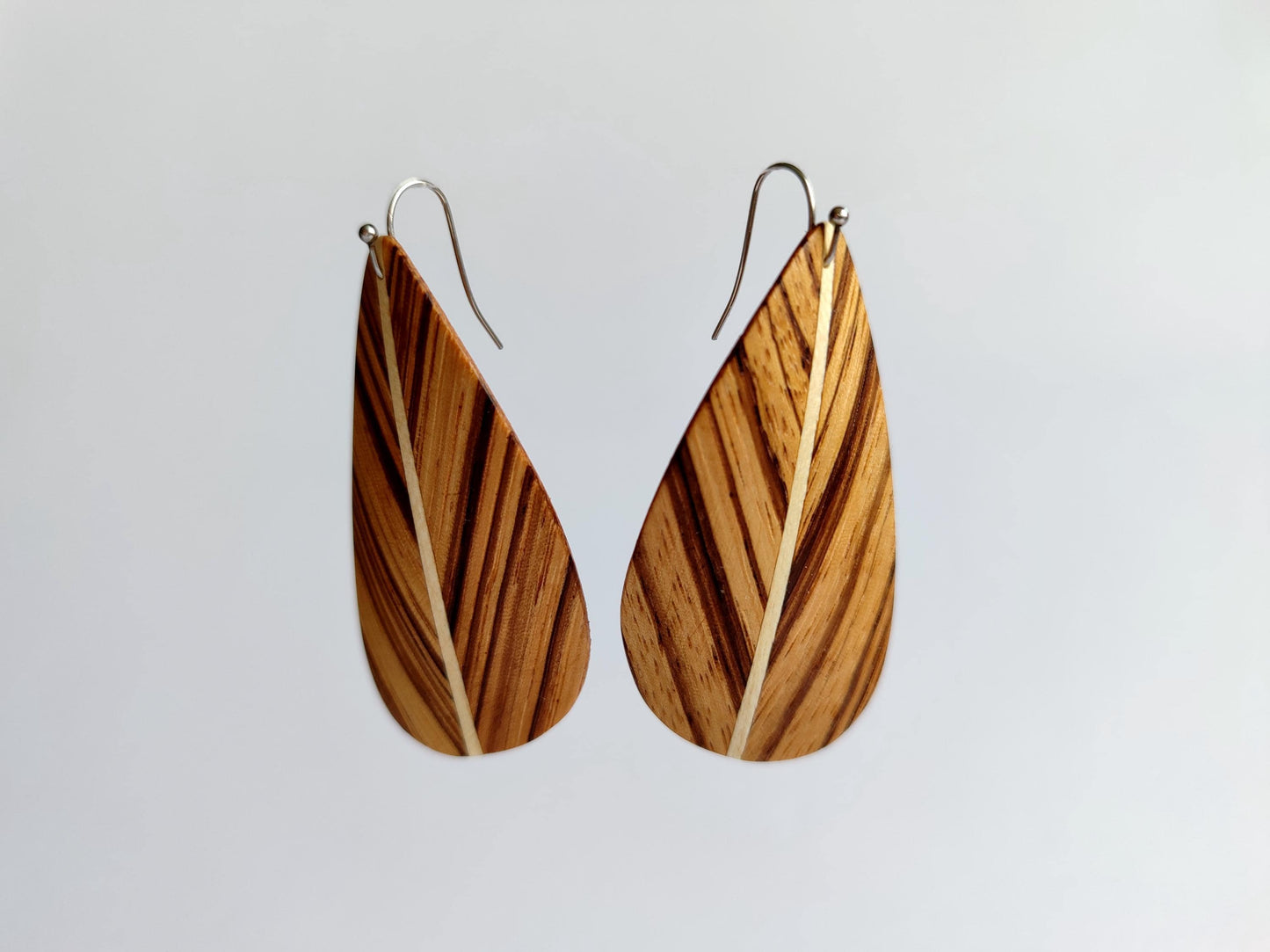 A pair of leaf dangle earrings with a natural wood grain pattern and silver fishhook wires, shown against a plain light gray background.