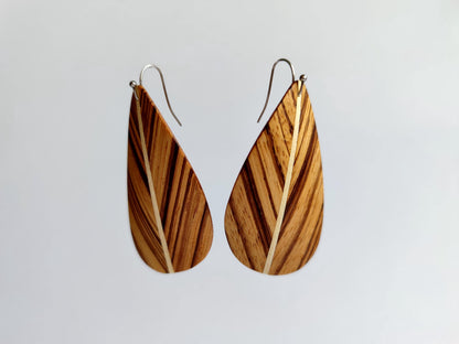 A pair of leaf dangle earrings with a natural wood grain pattern and silver fishhook wires, shown against a plain light gray background.