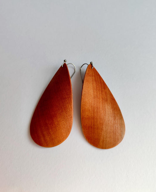 A pair of teardrop-shaped wooden dangle earrings with a warm reddish-brown finish and silver fishhook ear wires